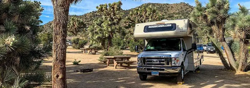 RV parked in basic campground with picnic table and fire ring