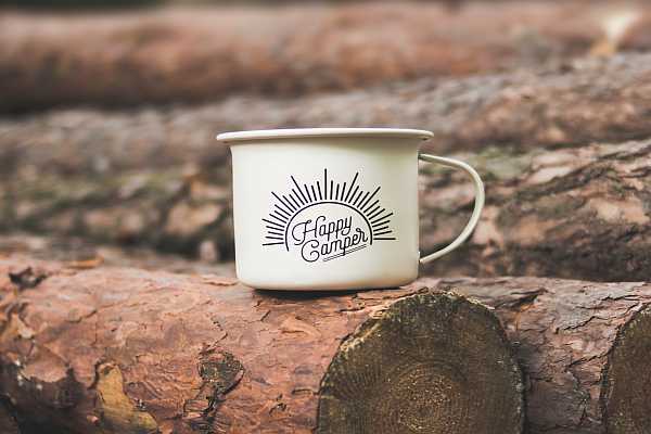 Coffee mug with logo for Happy Camper sitting atop of wooden log