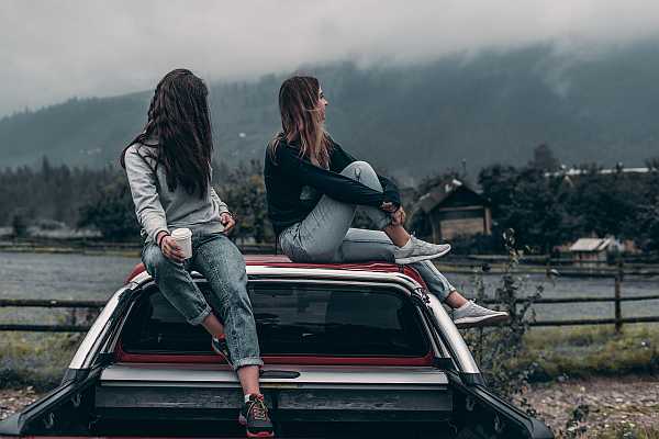 Two millennial women sitting on the roof and bed of a truck