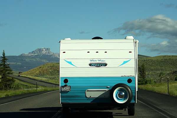 Back of a white and turquoise blue older RV on a country road