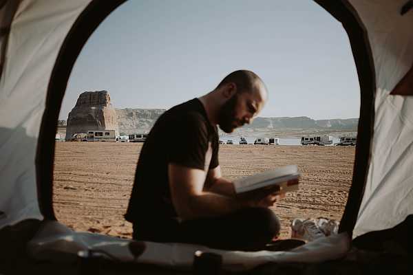 Image of a man reading a book with several RVs in the distance